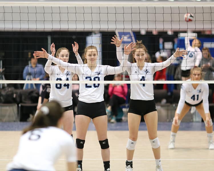Three club volleyball players standing ready at the net
